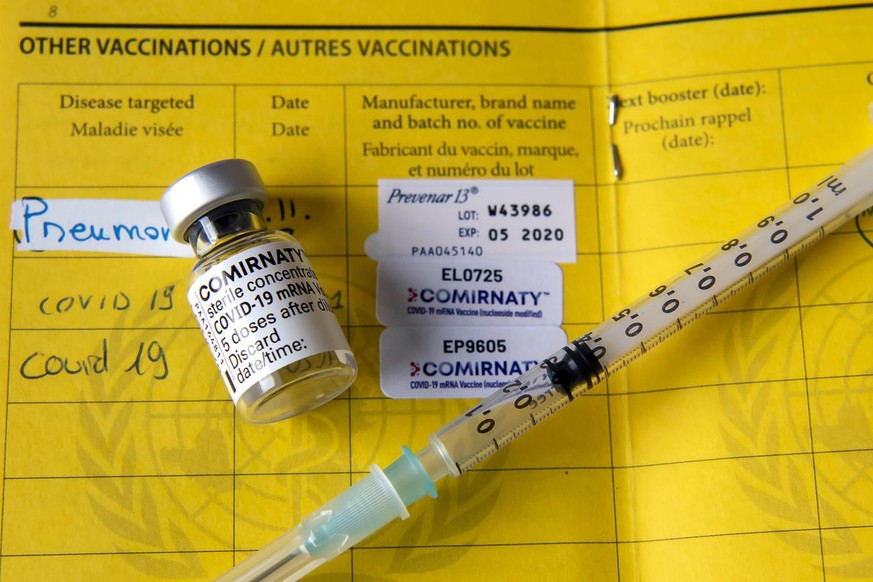 Une fiole du vaccin Pfizer-BioNTech et une seringue sont photographiees sur un carnet de l&#039;OMS de certificat international de vaccination ou de prophylaxie, faudra-t-il un jour un passeport vacci ...