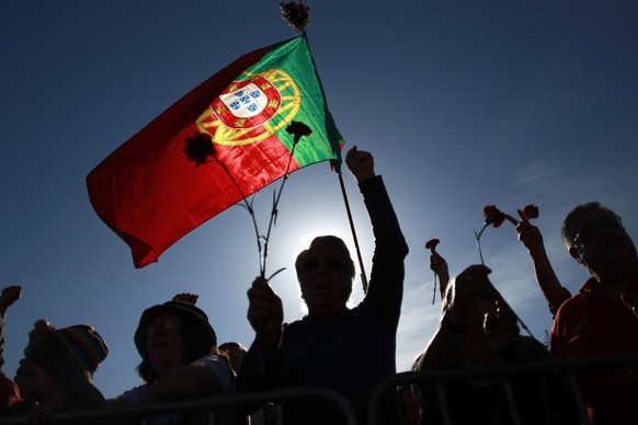 People holding red carnations and a Portuguese flag sing a protest song during a rally marking the international May Day, in Lisbon, Thursday, May 1, 2014. Beside defending labor rights, protesters sh ...