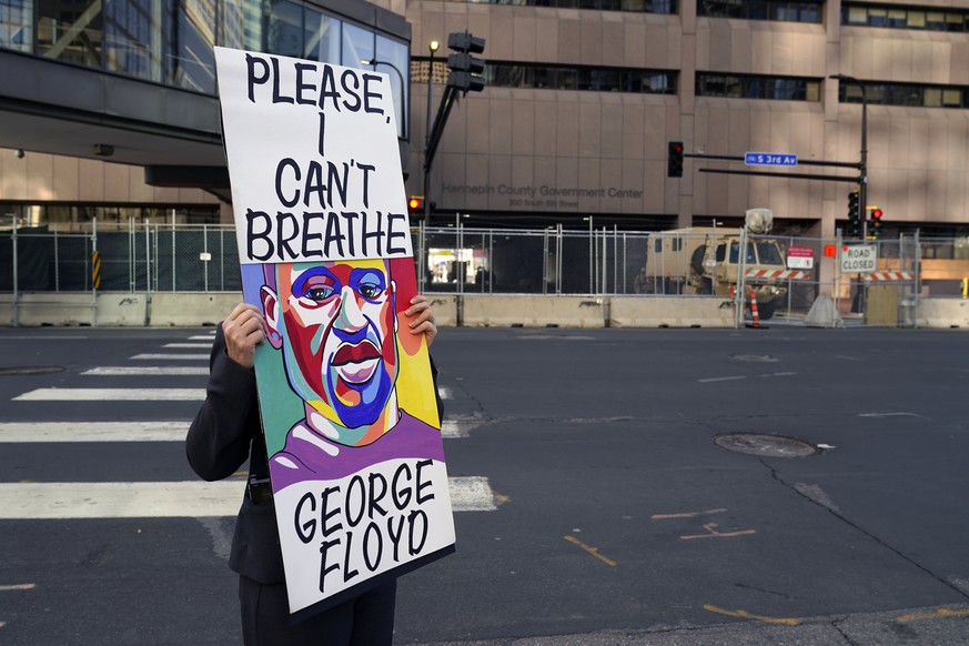 A protester holds a sign across the street from National Guard soldiers guarding the Hennepin County Government Center Tuesday, April 6, 2021, in Minneapolis where testimony continues in the trial of  ...