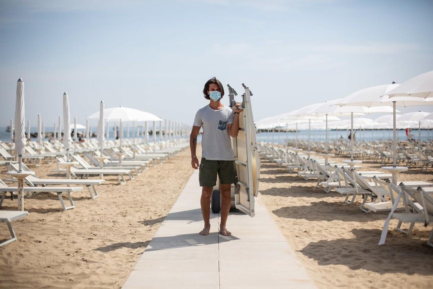 epa08439018 A worker wearing face mask sets up deck chairs and parasols during Phase 2 of the coronavirus emergency on the beach of Cesenatico, Italy, 23 May 2020. Italy&#039;s most popular beaches, i ...