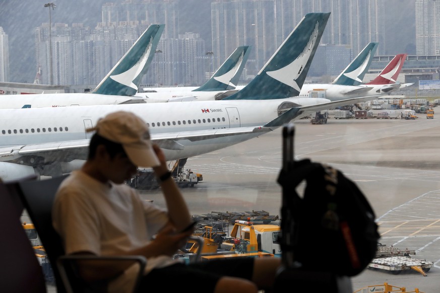 A traveller checks his smartphone while Cathay Pacific Airways planes park at the Hong Kong International Airport, Monday, Aug. 12, 2019. One of the world&#039;s busiest airports canceled all flights  ...