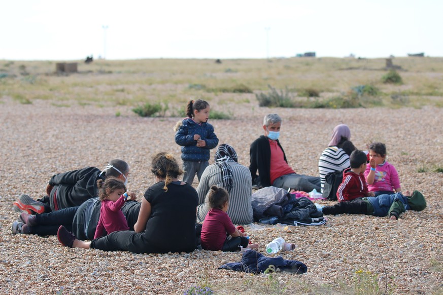 A group of migrants rest on the beach as they wait for Uk Border Force officials at Dungeness, southern England, Thursday Aug. 6 2020. The British government says it will strengthen border measures as ...