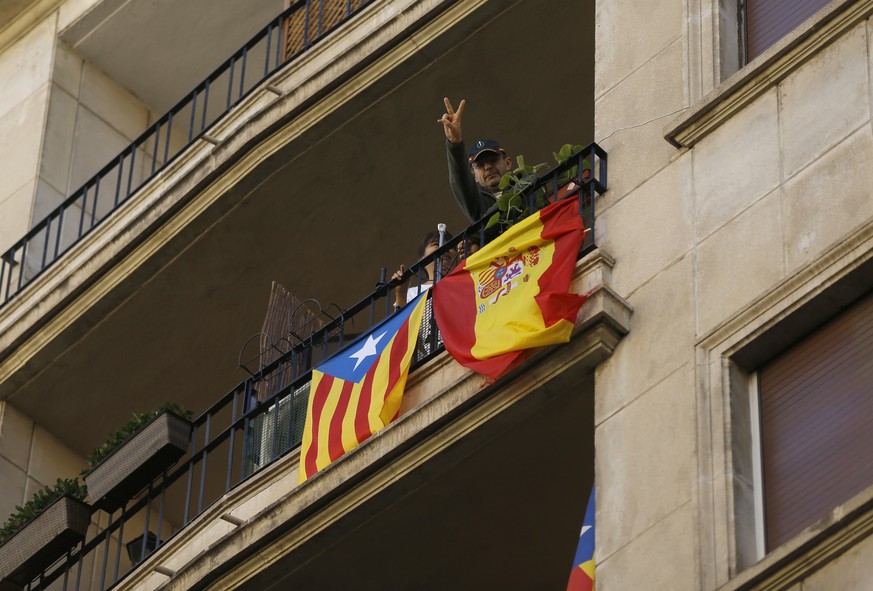 A man with a pro-independence Catalan flag and a Spanish flag hanging side by side on his balcony flashes the victory sign for the camera as he watches a march to protest the Catalan government&#039;s ...