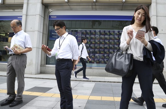In this Sept. 11, 2018, photo, people use smartphones in front of an electronic stock board of a securities firm in Tokyo. Asian shares were mostly higher Wednesday, Sept. 19, 2018, despite jitters ov ...