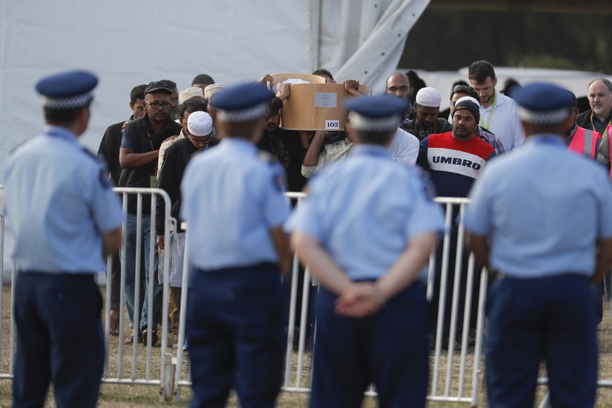 Police officials stand guard as mourners carry the body of a victim of the Friday, March 15 mosque shootings for a burial at the Memorial Park Cemetery in Christchurch, New Zealand, Friday, March 22,  ...
