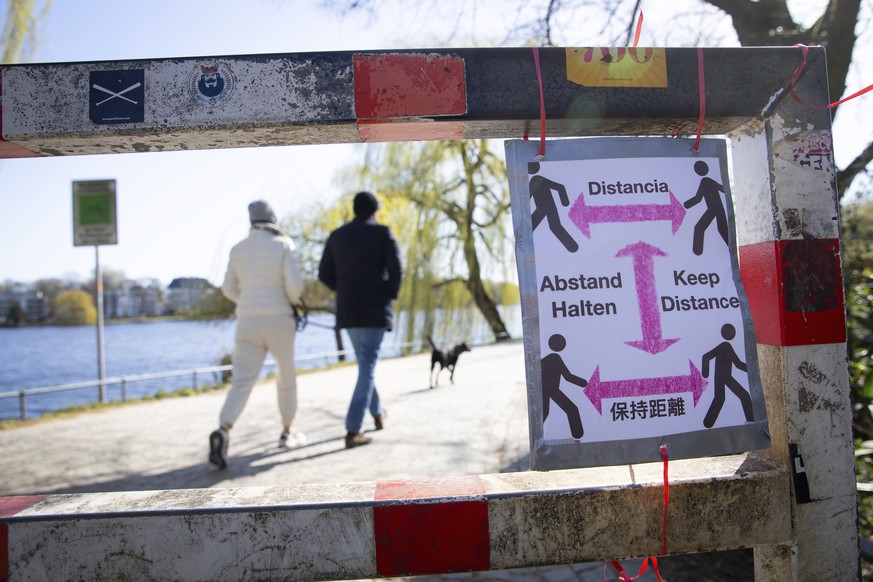 A self-made sign with the inscription &quot;Keep your distance&quot; in various languages is attached to the beginning of a path around the Alster river in Hamburg, Germany, Monday, March 23, 2020. In ...