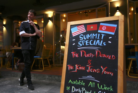 In this Feb. 24, 2019, photo, Durty Bird restaurant owner Colin Kelly stands next to a menu offering Trump-Kim summit special burgers in Hanoi, Vietnam. The summit this week between Kim Jong Un and Do ...