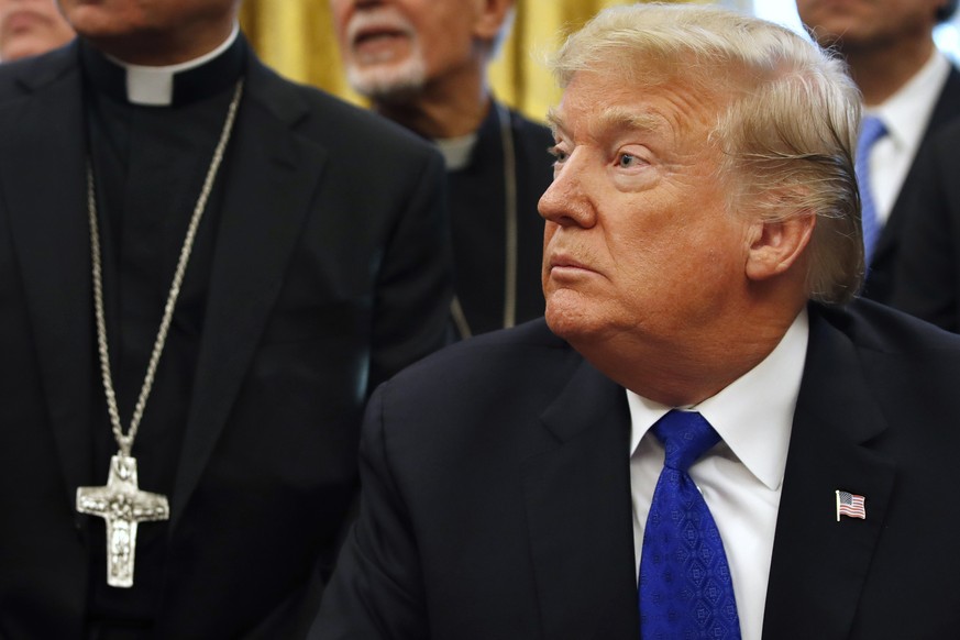 President Donald Trump sits at the Resolute desk, surrounded by members of clergy, to sign H.R. 390, the &quot;Iraq and Syria Genocide Relief and Accountability Act of 2018,&quot; in the Oval Office o ...