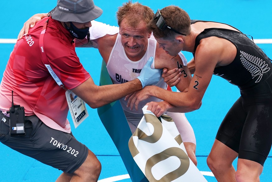 epa09365634 Winner Kristian Blummenfelt (C) of Norway is helped by a volunteer and third placed Hayden Wilde of New Zealand after the Men&#039;s Triathlon race of the Tokyo 2020 Olympic Games at the O ...