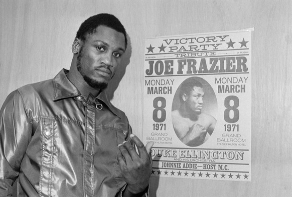 ARCHIV: Heavyweight champ Joe Frazier poses by a poster advertising his &quot;victory party&quot; as he leaves his dressing room after a final public workout in Philadelphia before his title defense b ...
