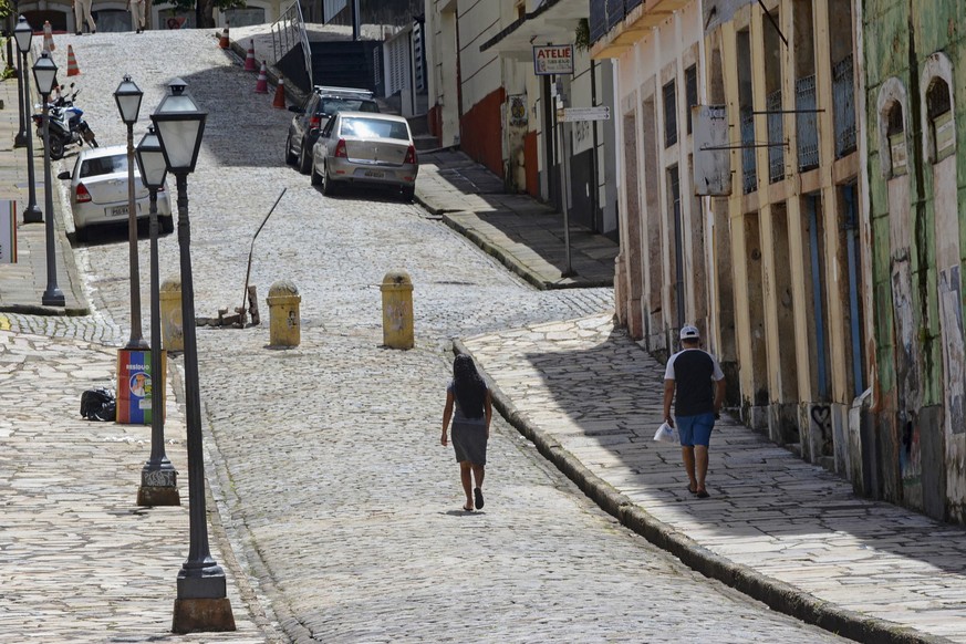 People walk in an empty street during a lockdown imposed by the government to help stop the spread of the new coronavirus in the historic district of downtown Sao Luis, in the northeastern state of Ma ...