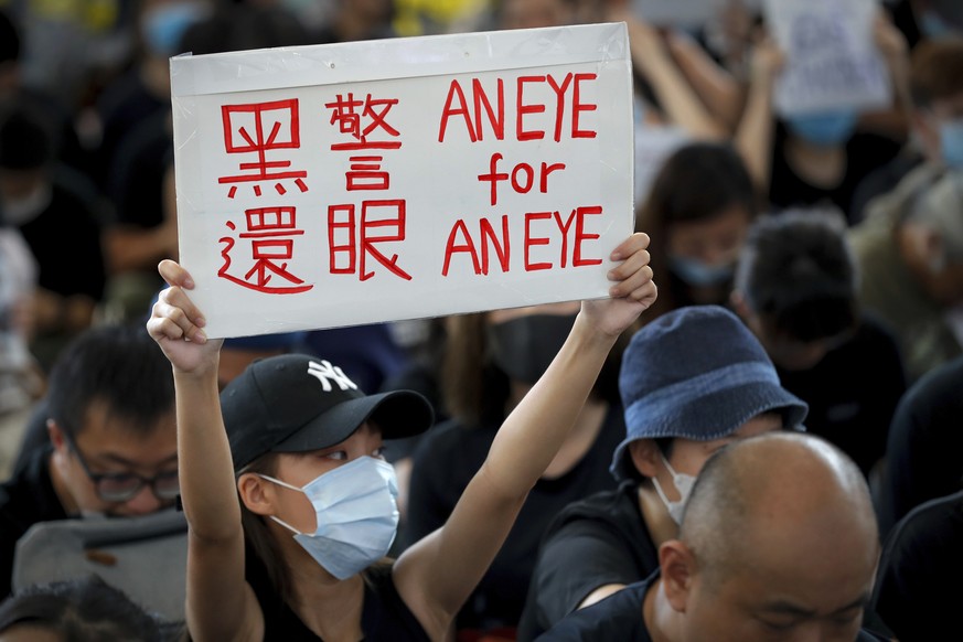 A woman holds a placard which reads &quot;Black police, Return eye,&quot; during a sit-in protest at the arrival hall of the Hong Kong International Airport in Hong Kong, Monday, Aug. 12, 2019. It is  ...