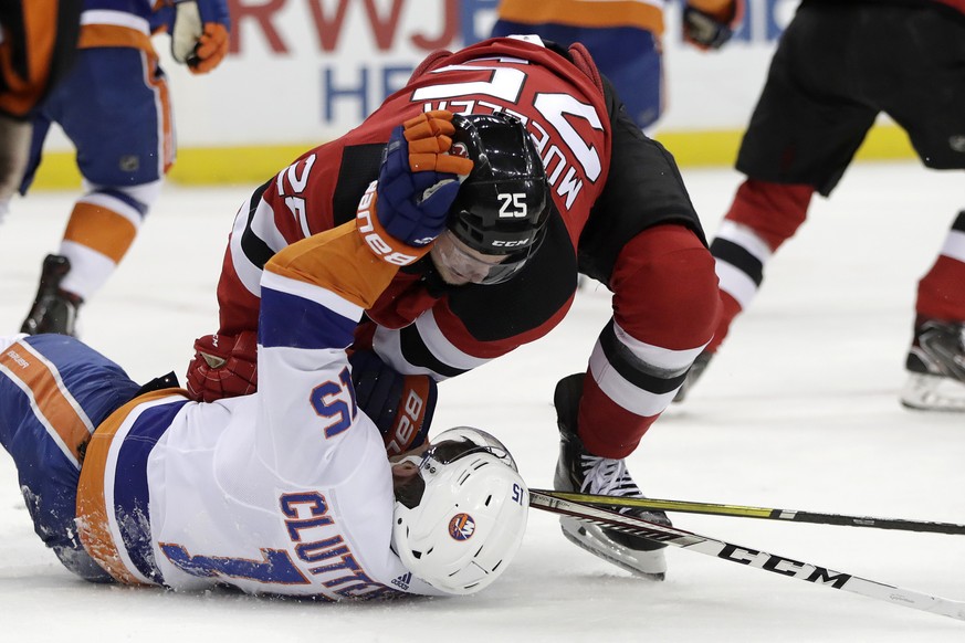 New York Islanders right wing Cal Clutterbuck (15) and New Jersey Devils defenseman Mirco Mueller (25), of Switzerland, grab at each other while competing for possession of the puck during the first p ...