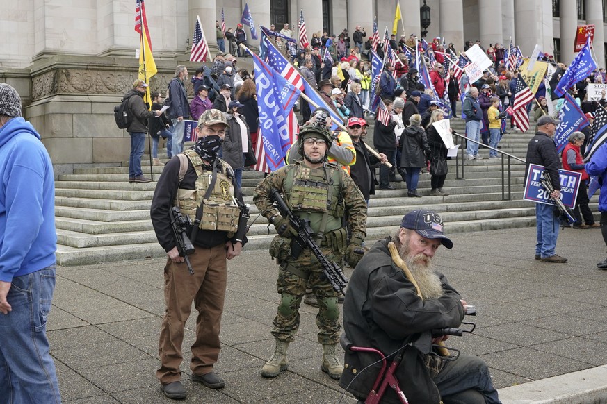 In this photo taken Jan. 6, 2021 at the Capitol in Olympia, Wash., two men stand armed with guns at a protest supporting President Donald Trump and against the counting of electoral votes in Washingto ...