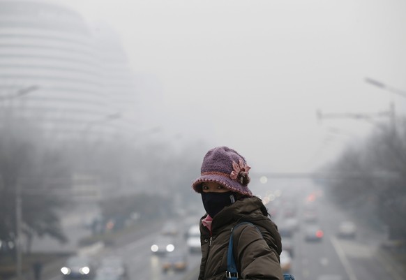 epa04098578 A woman wearing a protective mask walks along a commuter bridge overlooking a main road amidst smog in Beijing, China, 24 February 2014. Due to smog alerts, a city in northern China has ba ...