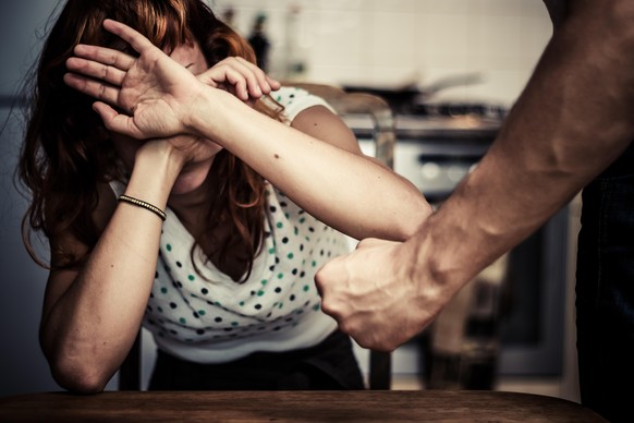 Konzept der häuslichen Gewalt mit verängstigter und verletzter Frau, die vor einem gewalttätigen Mann schützt