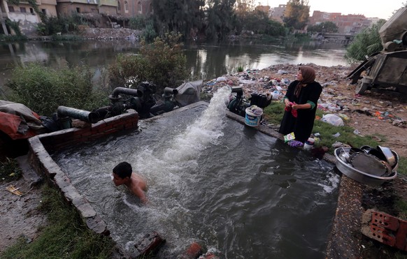 epa04852420 An Egyptian woman wash plates and utensils as a boy plays inside water pumped for irrigation from the Rosettaat of the Nile River, in the village of Dalgamon, Tanta, some 120km north of Ca ...