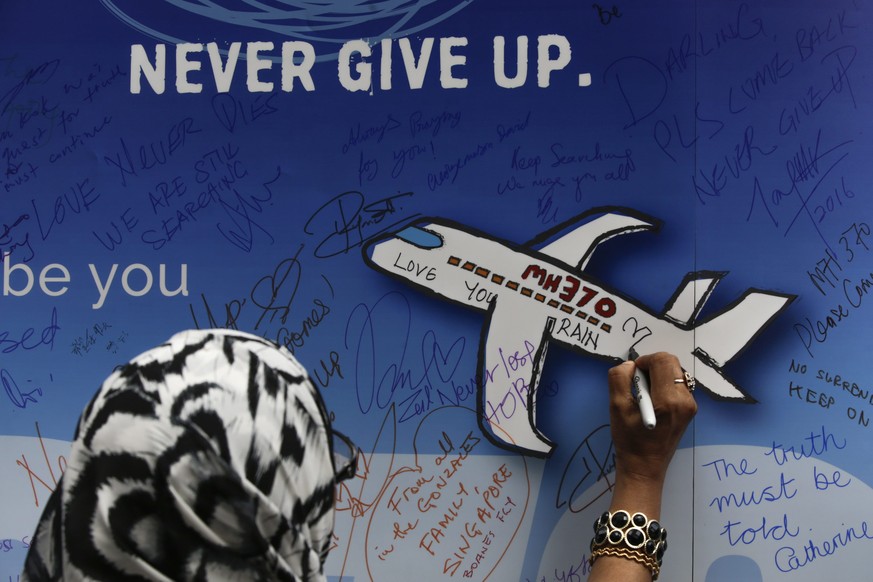 epa05197357 A woman writes messages for the passengers of missing Malaysia Airlines flight MH370 on a banner during a remembrance ceremony to mark the second anniversary of the plane&#039;s disappeara ...