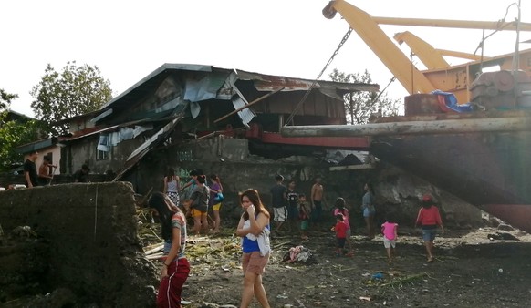 epaselect epa08089584 Villagers walk around a cargo ship washed ashore and a damaged home on Christmas day in the typhoon-hit city of Ormoc, Philippines, 25 December 2019. Typhoon Phanfone, (locally k ...