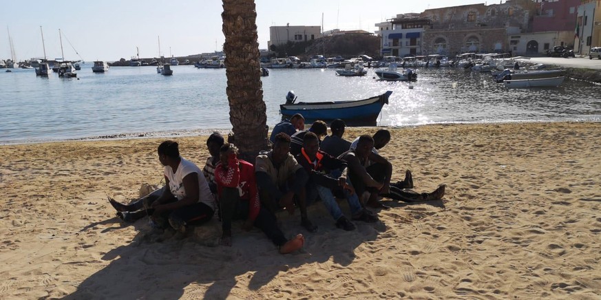 epa08564724 A group of sub-Saharan migrants sit around a tree at the beach after arriving in Lampedusa, southern Italy, 24 July 2020. The group crossed the Mediterranean in a small boat from Tunisian  ...