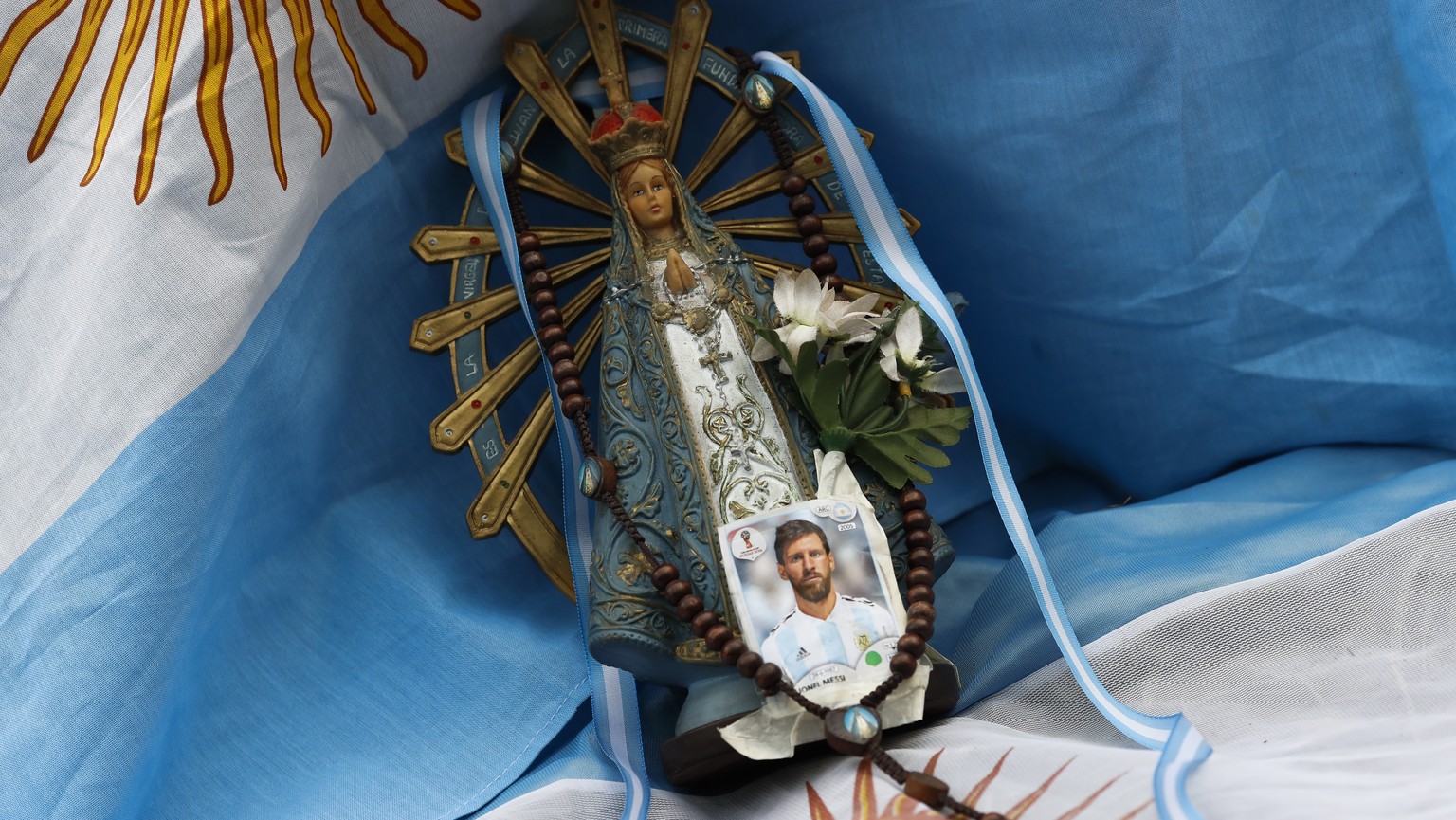 epa06842885 A photograph of the player Lionel Messi is placed next to the figure of a virgin on an Argentinian flag during as Argentinian fans watch the match between Argentina and Nigeria at the 2018 ...