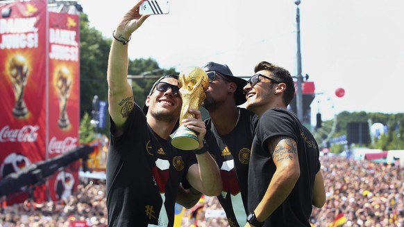 Germany&#039;s Lukas Podolski, Jerome Boateng and Mesut Oezil (L-R) pose for a &#039;selfie&#039; with the World Cup trophy during celebrations to mark the team&#039;s 2014 Brazil World Cup victory, a ...