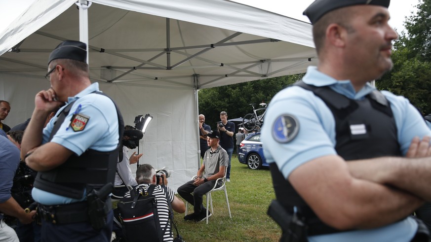 French police keep watch as four-time Tour de France cycling race winner Chris Froome of Britain, center rear, answers questions during a TV interview after a press conference in Saint-Mars-la-Reorthe ...