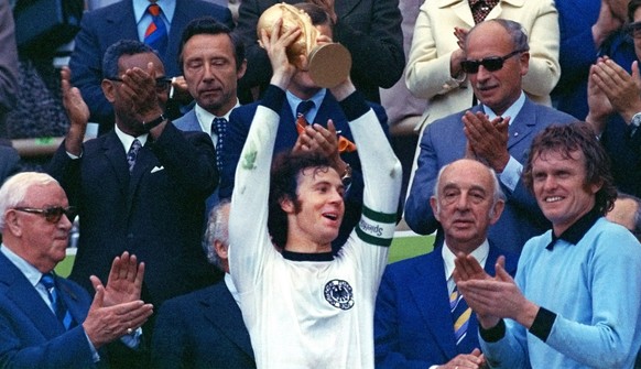 Surrounded by applauding spectators, Franz Beckenbauer, center, team captain of the winning German national soccer team at the 1974 world soccer championship presents the trophy in Munich&#039;s, Germ ...