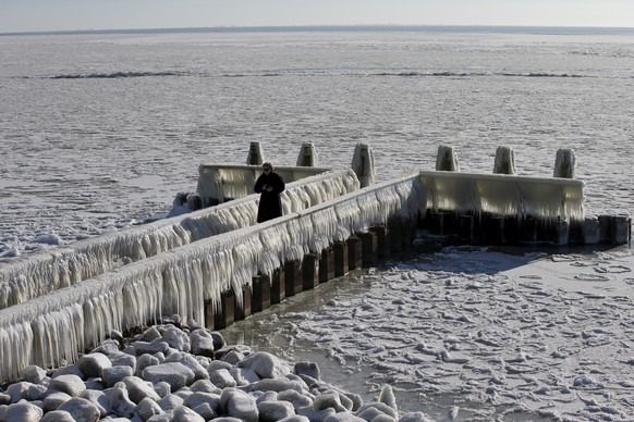 A woman takes pictures of icicles on a jetty at the Afsluitdijk, a dike separating IJsselmeer inland sea, and the Wadden Sea, Netherlands, Thursday, Feb. 11, 2021. The deep freeze gripping parts of Eu ...