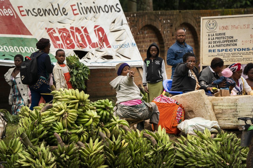 In this Sunday, July 14, 2019 photo, women sell bananas by an Ebola awareness poster reading &quot;together let&#039;s eliminate Ebola&quot; in Beni, Congo DRC. The World Health Organization has decla ...