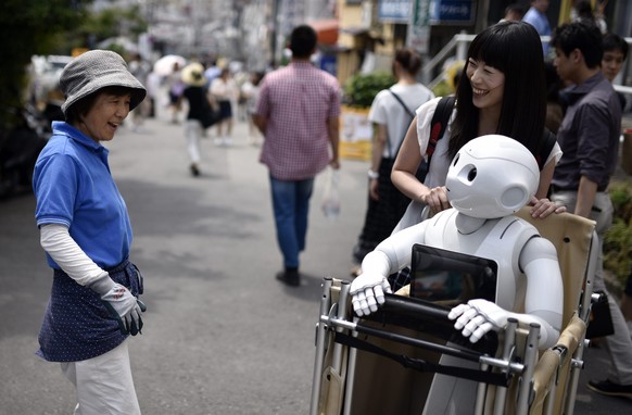epa05406533 (06/21) A woman reacts as she sees Tomomi Ota (R) pushing a cart loaded with her humanoid robot Pepper in Tokyo, Japan, 26 June 2016. Reaching 120cm in height and 28 kilograms in weight, P ...