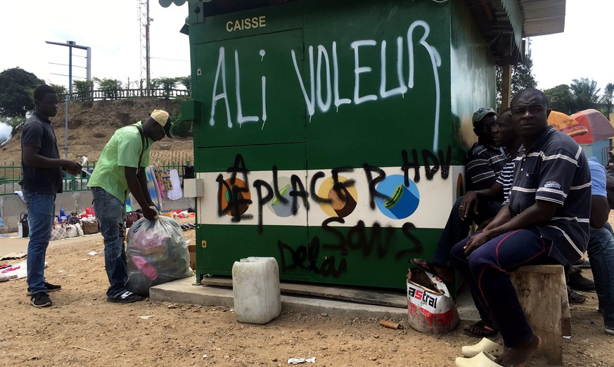 People sit next to graffiti that reads &quot;Ali Thief&quot;, referring to incumbent President Ali Bongo, in Libreville, Gabon, September 24, 2016. Picture taken September 24, 2016. REUTERS/Marco Truj ...