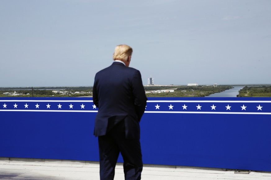 President Donald Trump looks on as a SpaceX Falcon 9, with NASA astronauts Doug Hurley and Bob Behnken in the Crew Dragon capsule, sits on Launch Pad 39-A at the Kennedy Space Center in Cape Canaveral ...