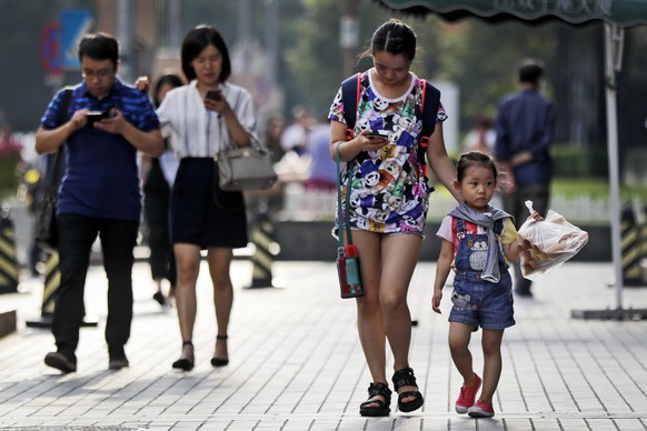 Pedestrians view their smartphones as they walk along a sidewalk in Beijing, Wednesday, Aug. 9, 2017. China has one of the world&#039;s largest mobile phone market and become more and more popular amo ...