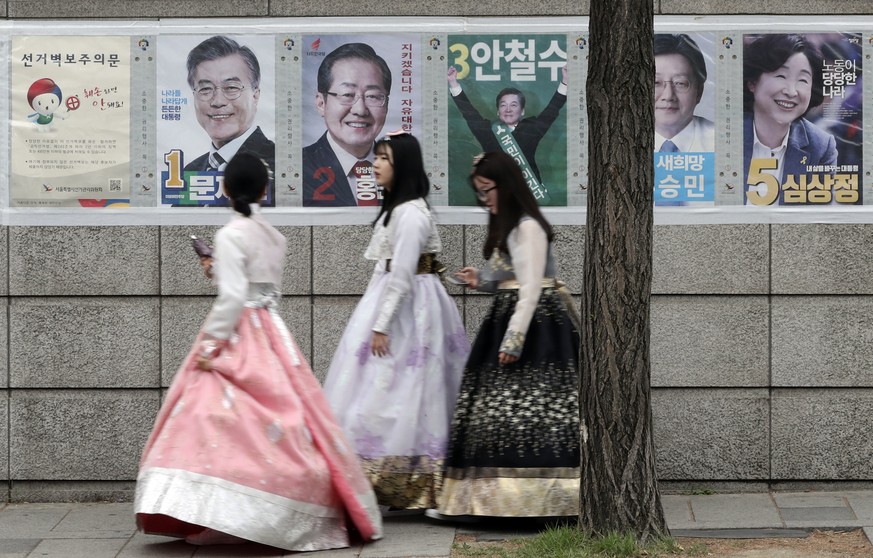 Women walk by posters showing candidates for the presidential election in Seoul, South Korea, Tuesday, May 9, 2017. South Koreans voted Tuesday for a new president, with victory widely predicted for a ...