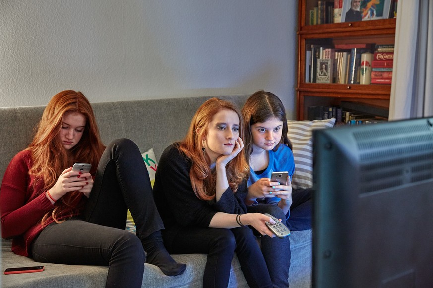 [Symbolic Image, Staged Picture, ] Sisters sitting on a couch in the living room use their smart phones while watching TV, photographed in Lucerne, Switzerland, on December 13, 2015. (KEYSTONE/Christo ...
