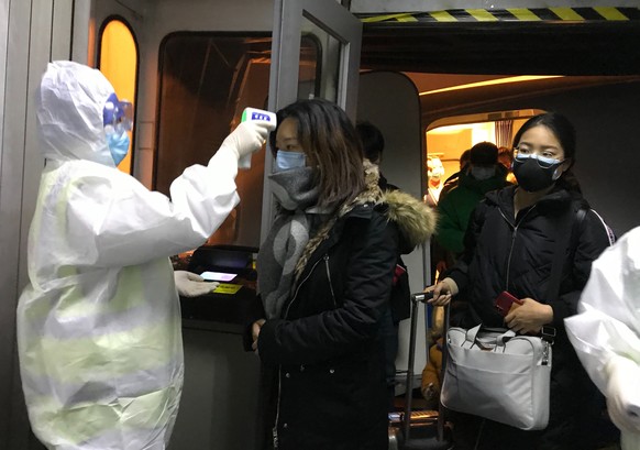 Health Officials in hazmat suits check body temperatures of passengers arriving from the city of Wuhan Wednesday, Jan. 22, 2020, at the airport in Beijing, China. Nearly two decades after the disastro ...