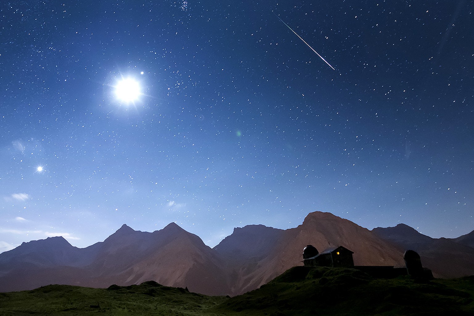 Eine sehr helle Sternschnuppe leuchtet am Nachthimmel ueber der Sternwarte in Arosa, in der Nacht auf Sonntag, 12. August 2012. Links scheint der Mond. Hinten die Berge Medergerflue, Tiejerflue, Furka ...