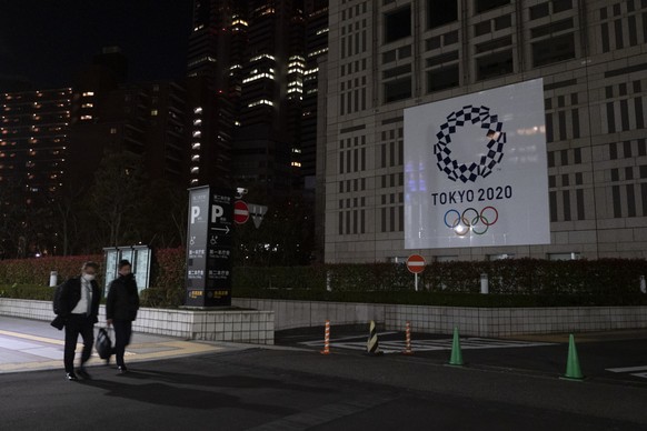 Two men walk past a large banner promoting the Tokyo 2020 Olympics in Tokyo, Tuesday, March 24, 2020. IOC President Thomas Bach has agreed &quot;100%&quot; to a proposal of postponing the Tokyo Olympi ...