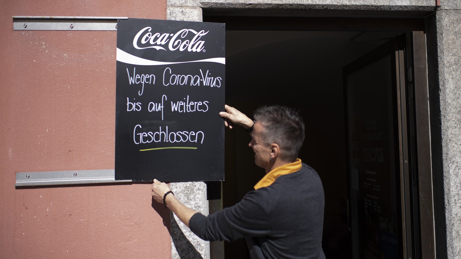 Chef Linus Caduff haengt ein Schild vor das Cafe Arcas mit der Aufschrift &quot;Wegen Coronavirus bis auf weiteres geschlossen&quot;, am Montag, 16. Maerz 2020, in Chur. Die Buendner Regierung hat bes ...