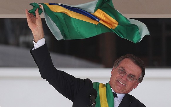 epa07257476 Brazilian newly inaugurated President Jair Bolsonaro waves the national flag as he delivers a speech after receiving the presidential band during his inauguration ceremony at the Planalto  ...