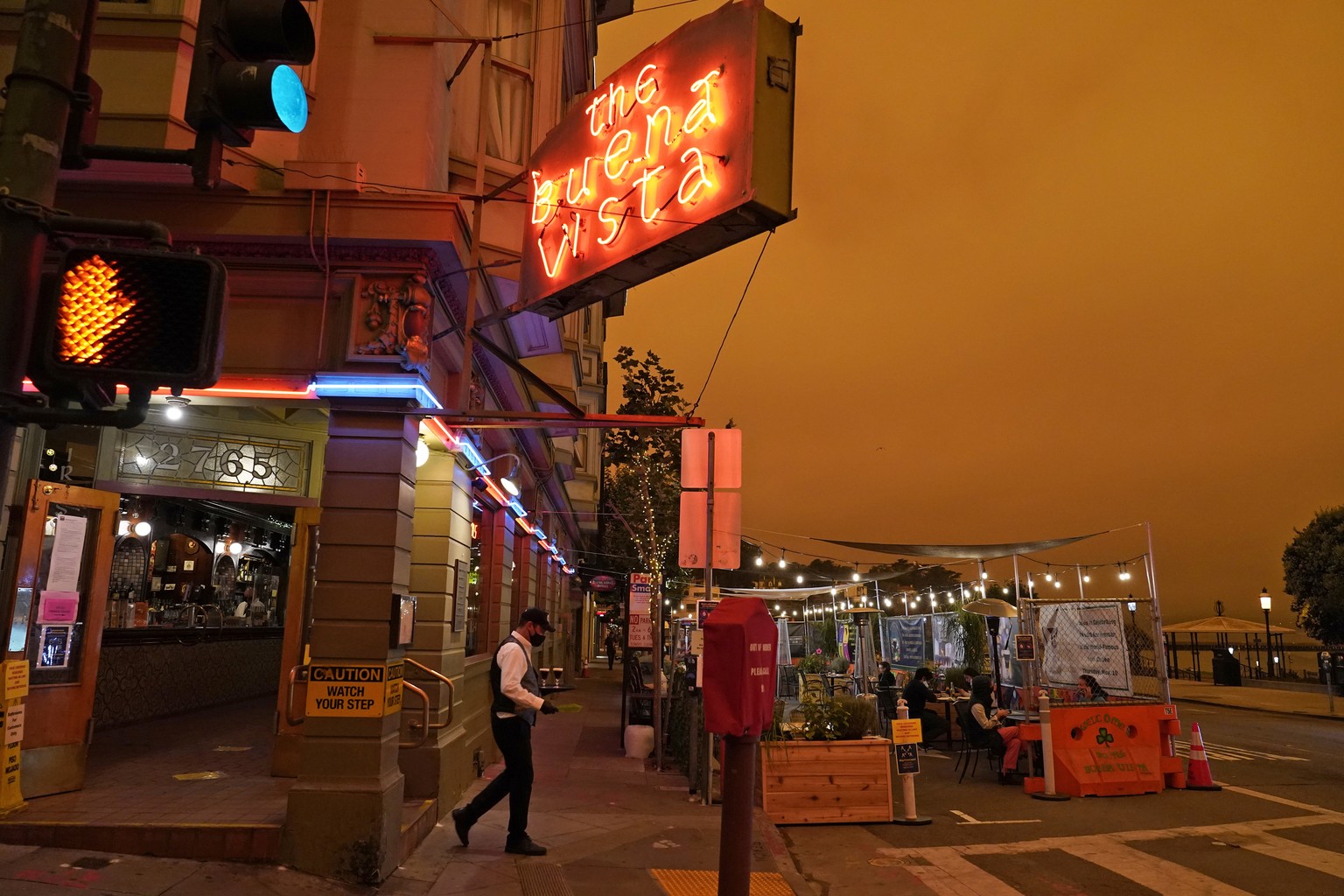 Under darkened skies from wildfire smoke, a waiter carries a tray of Irish Coffee to people having lunch at the Buena Vista Cafe Wednesday, Sept. 9, 2020, in San Francisco. People from San Francisco t ...