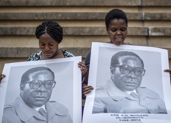 FILE - In this Sept. 14, 2019, file photo, women in the stands hold posters of former president Robert Mugabe at his state funeral at the National Sports Stadium in the capital Harare, Zimbabwe. (AP P ...