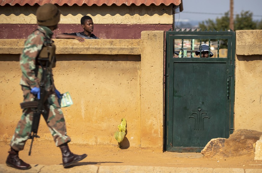 Residents look on as a soldier patrols on the streets of Soweto, South Africa, Thursday, April 23, 2020, as the country remains in lockdown for a fourth week in a bid to combat the spread of the coron ...