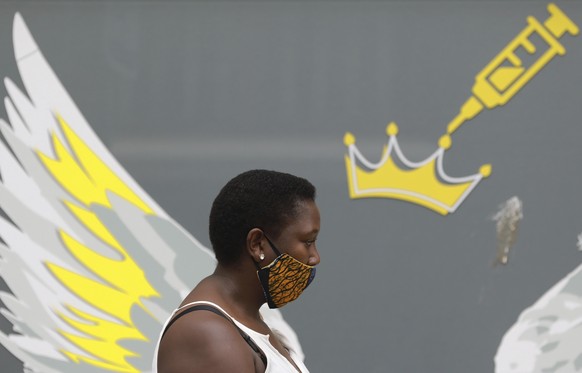 A woman wears a mask to protect against coronavirus as the passes a wall mural depicting a syringe , n Cape Town, South Africa, Thursday, Jan. 21, 2021. South Africa is preparing a hero���s welcome Mo ...