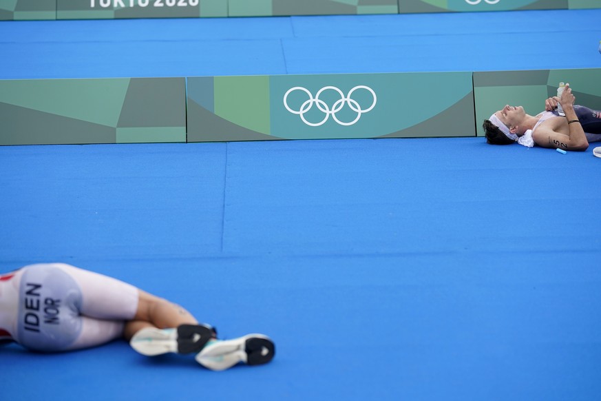 Gustav Iden of Norway, left, and Kevin McDowell of the United States (52) lie on the ground in exhaustion after finishing the men&#039;s individual triathlon at the 2020 Summer Olympics, Monday, July  ...