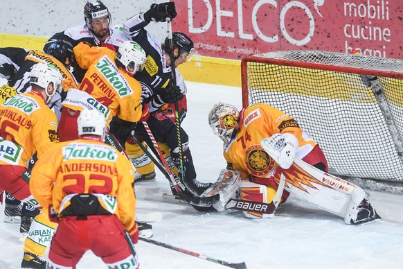 Ambri&#039;s player Johnny Kneubuehler, left, fightS for the puck with Tiger&#039;s goalkeeper Ivars Punnenovs, right, during the match of National League A (NLA) Swiss Championship 2020/21 between HC ...