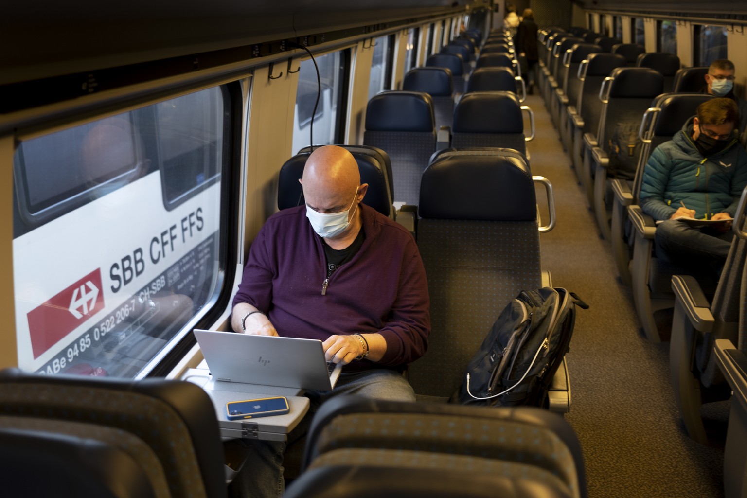 Passenger wearing protective mask works on a laptop as he rides a SBB CFF FFS train during the coronavirus disease (COVID-19) outbreak, in Biel Bienne, Switzerland, Tuesday, March 23, 2021. Switzerlan ...