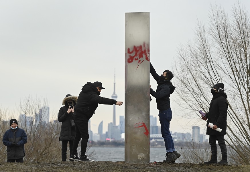 A man tries to clean graffiti from the vandalized monolith as people look at a metallic monolith that appeared on the shorelines of Humber Bay Park during the COVID-19 pandemic in Toronto onFriday, Ja ...