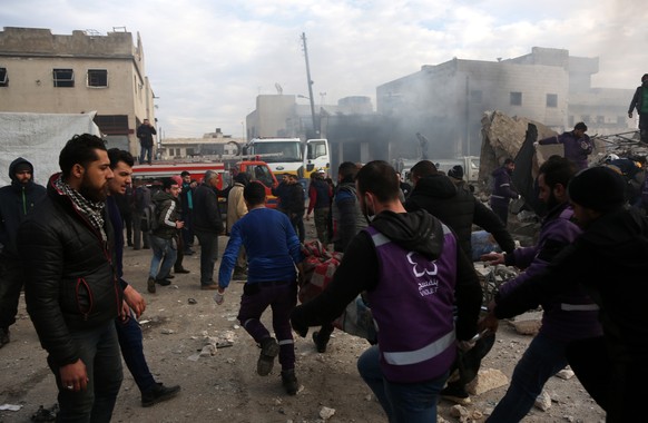 epa08130658 Rescuers carry bodies of victims at the site of airstrike targeting the center in the industrial area in the east of Idlib, Syria, 15 January 2020. According to media reports, at least 15  ...